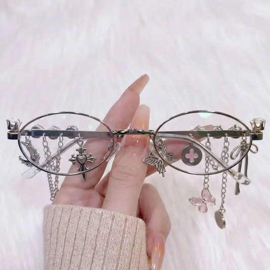 Unleash your alt aesthetic with our Y2K gothic oval glasses! Featuring a silver metal frame, rhinestone rim, and edgy dangling cross & butterfly charm chains. Perfect for dark coquette, grunge, and cyber goth style lovers. Shop today!